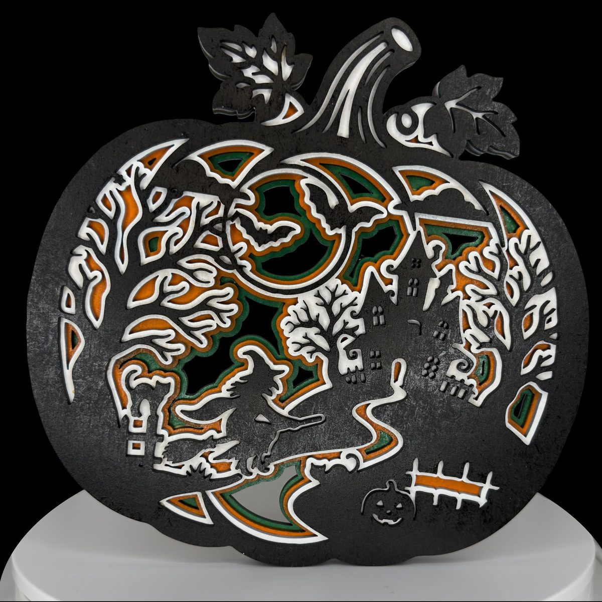 A pumpkin-shaped layered piece, black on the outside, holding a haunted house, a witch on a broom and bare trees cut through to orange and green layers beneath.