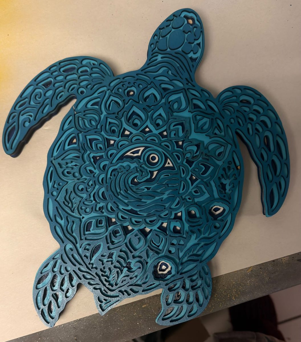A sea turtle cut as a layered piece in shades of teal and blue, the pattern of its shell stepped down through the layers.